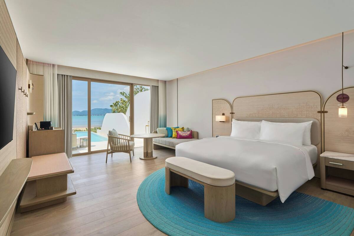 A modern hotel room with a large bed, a desk, a chair, and a view of the ocean.