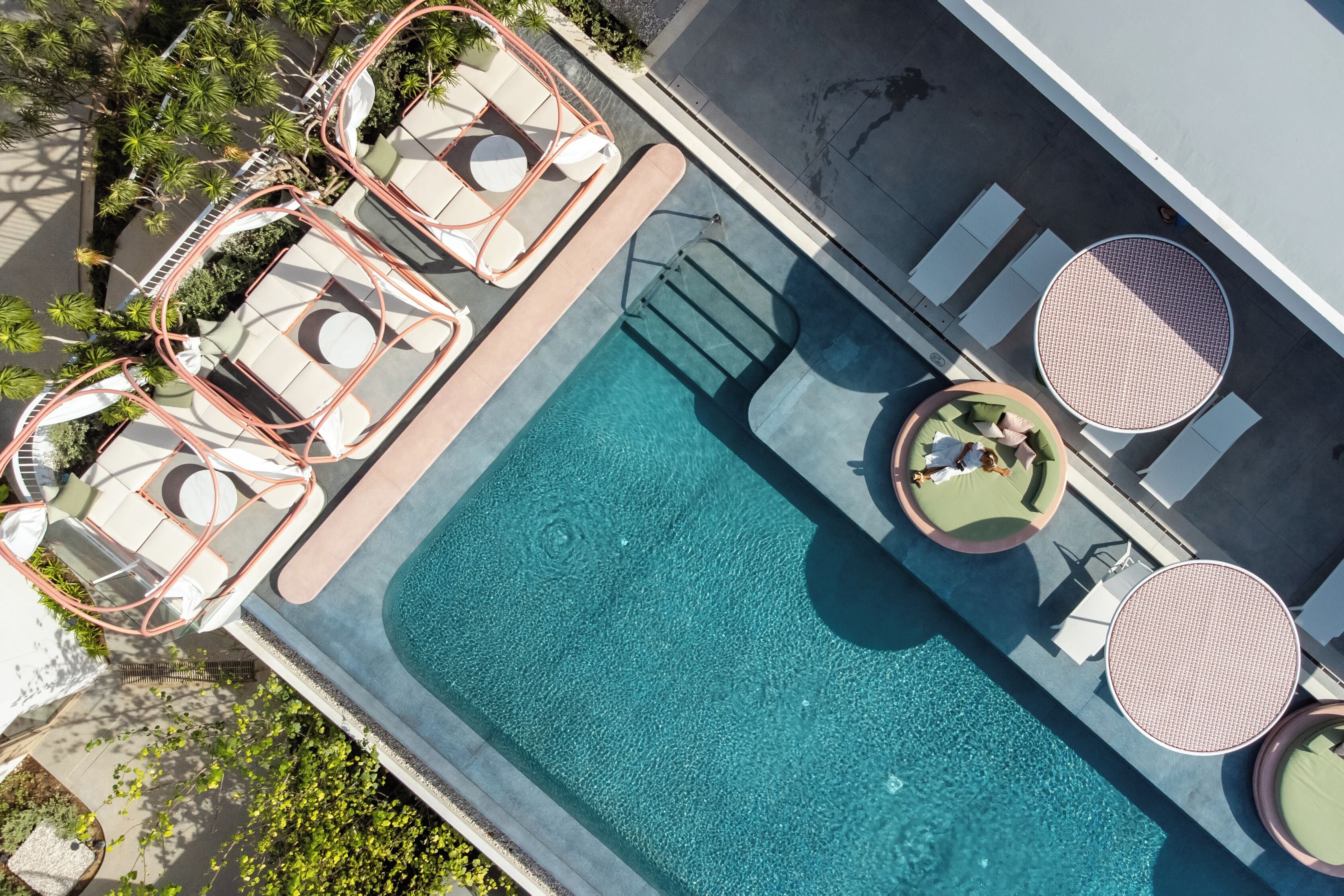Vista aérea de una piscina con sillas de descanso y mesas, rodeada de follaje.