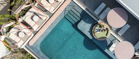 An aerial view of a swimming pool with lounge chairs and tables, surrounded by greenery.