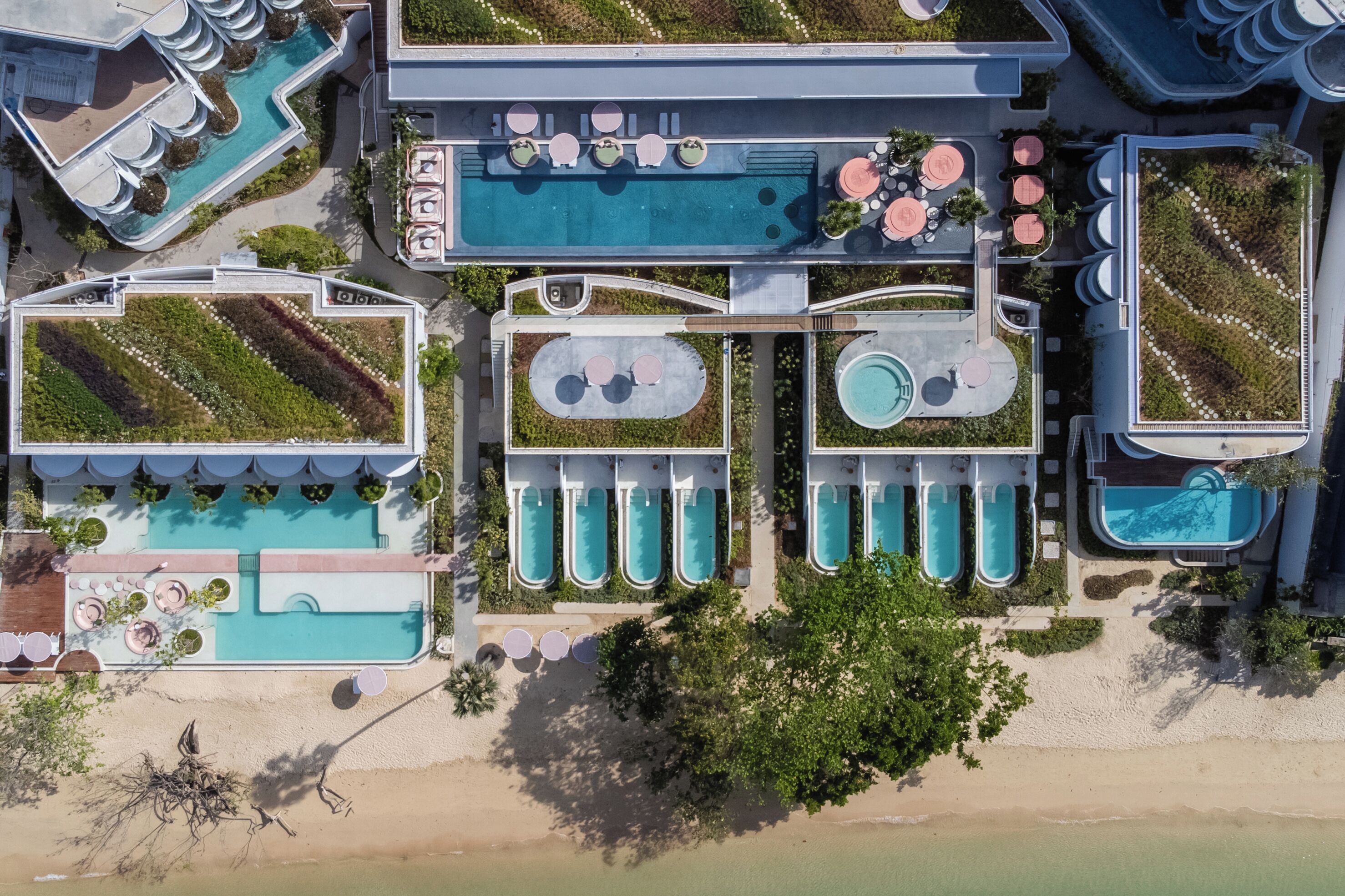 Vista aérea de un complejo turístico con múltiples piscinas, una zona de playa y jardines ajardinados.