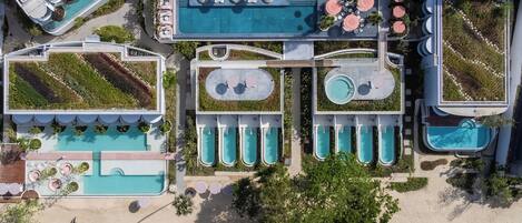 Vista aérea de un complejo turístico con múltiples piscinas, una zona de playa y jardines ajardinados.