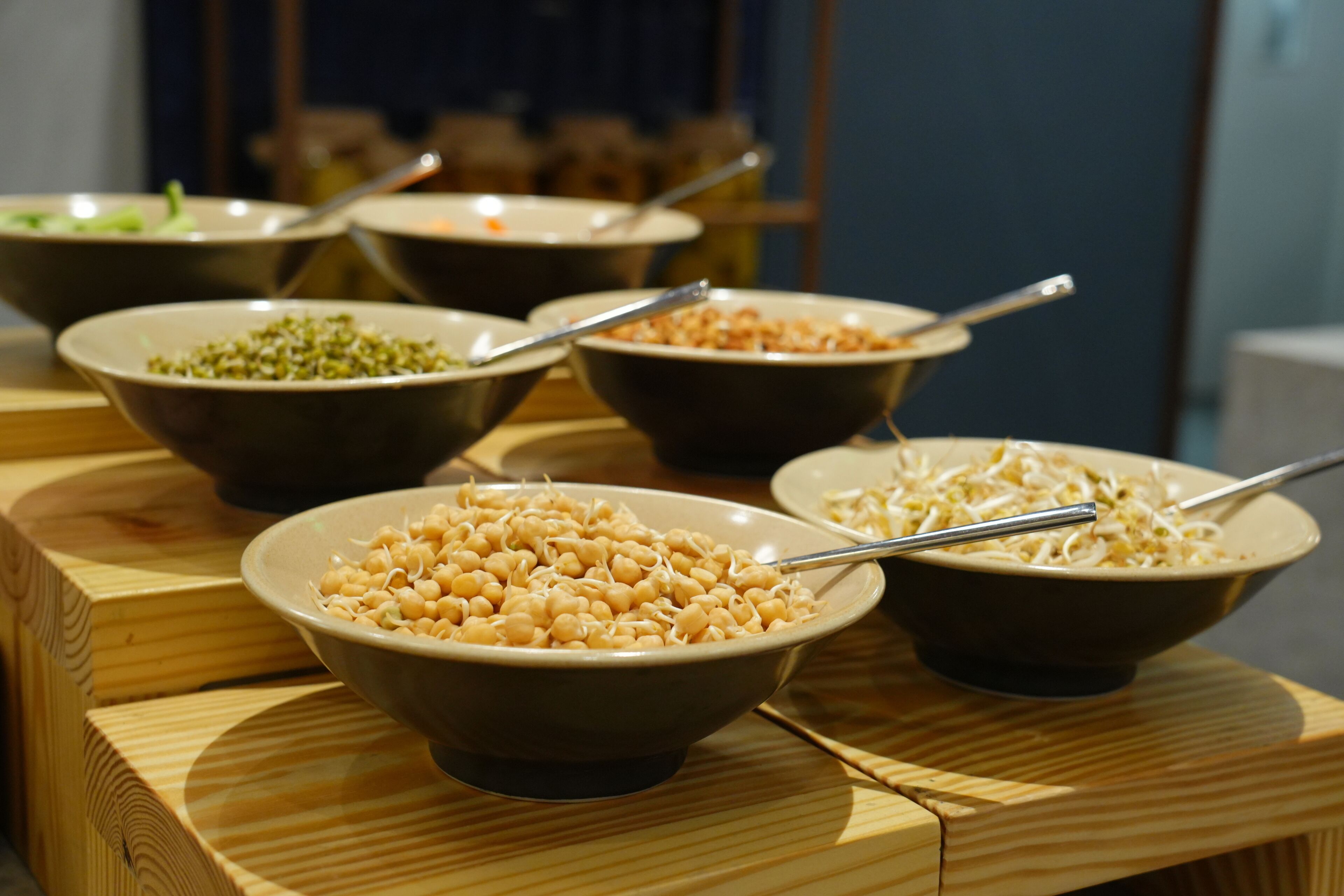 Una mesa de madera con varios recipientes de comida, incluyendo un tazón de garbanzos y un tazón de fideos.