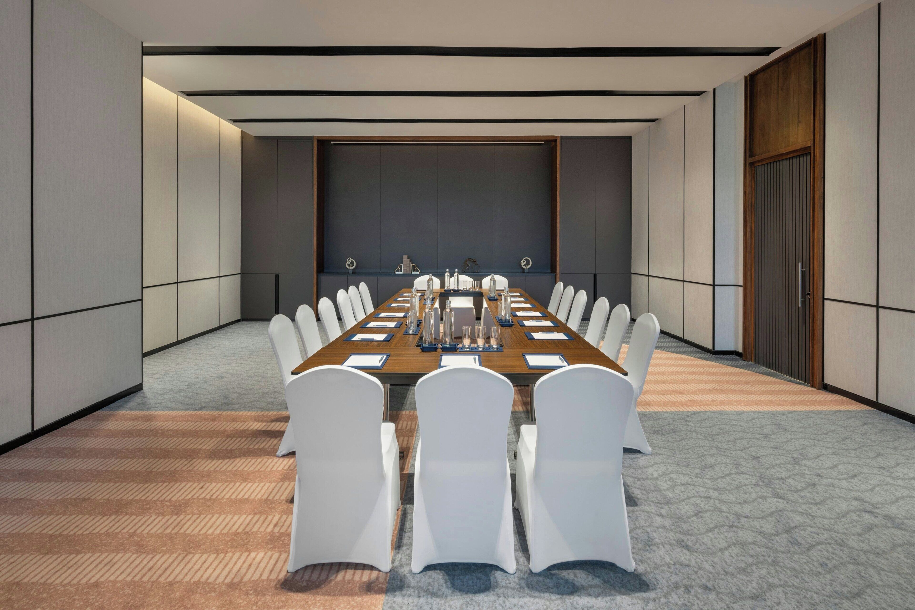 A conference room with a long table, white chairs, and a neutral color scheme.