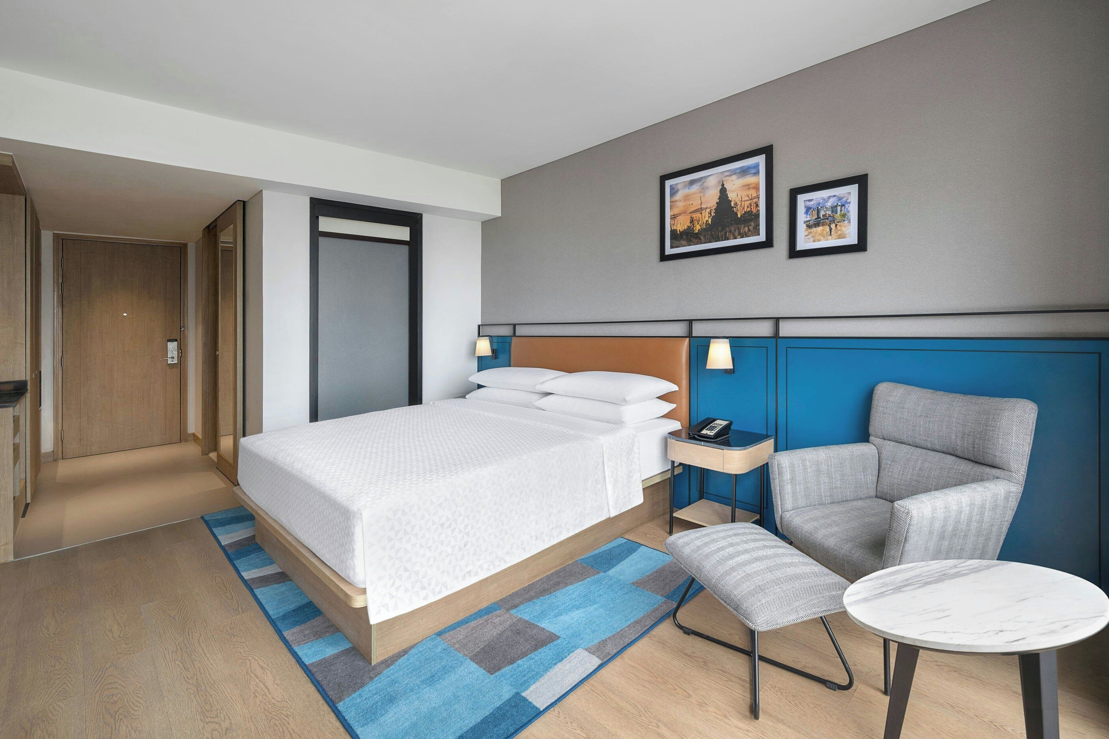 Een hotelkamer met een bed, een stoel, een klein tafeltje en een nachtkastje.