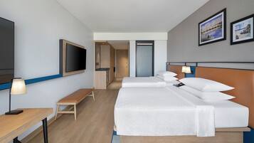 A hotel room with a bed, bedside tables, a TV, a bench, and a door leading to a bathroom.