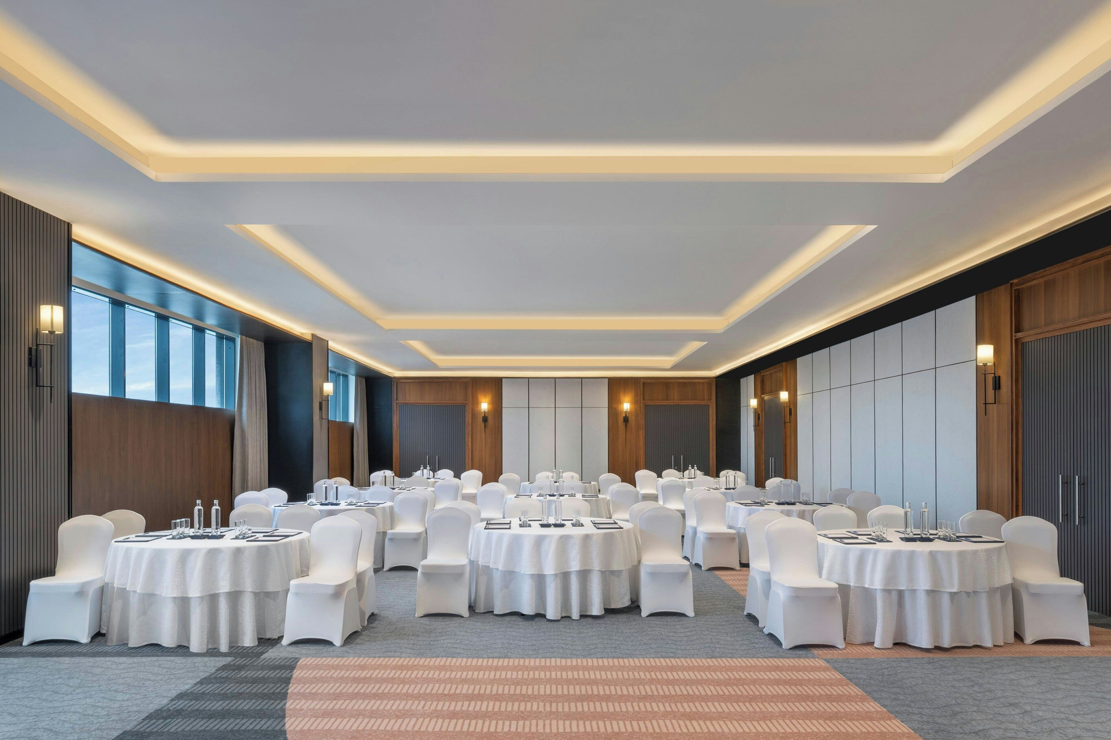 A conference room with multiple round tables, white chairs, and a carpeted floor.
