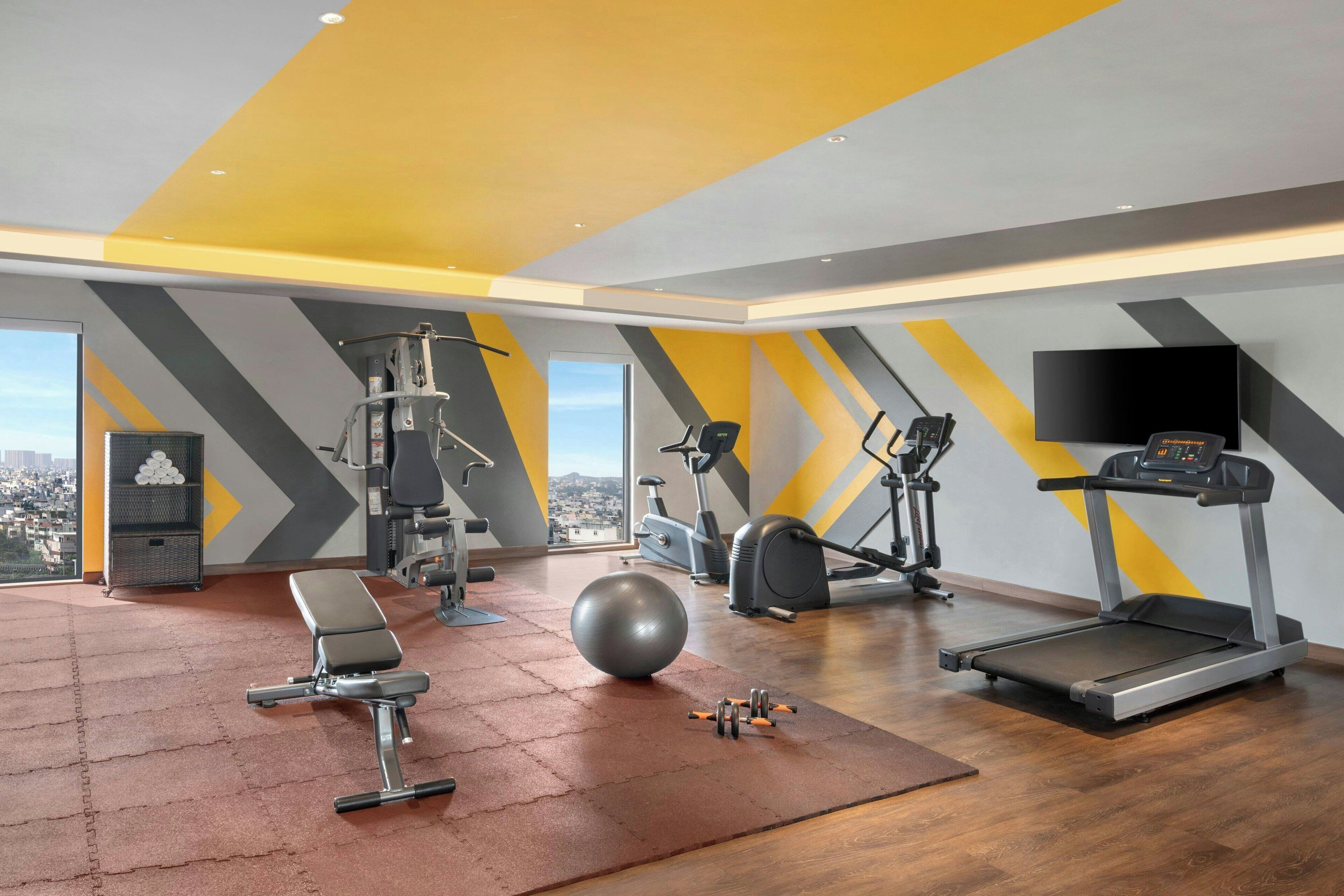A modern gym with various exercise equipment, a bench, a ball, and a treadmill.
