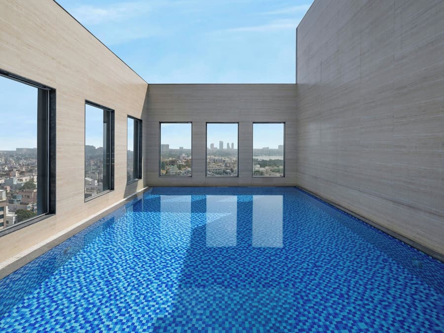 A modern indoor pool with a city view, large windows, and a tiled floor.