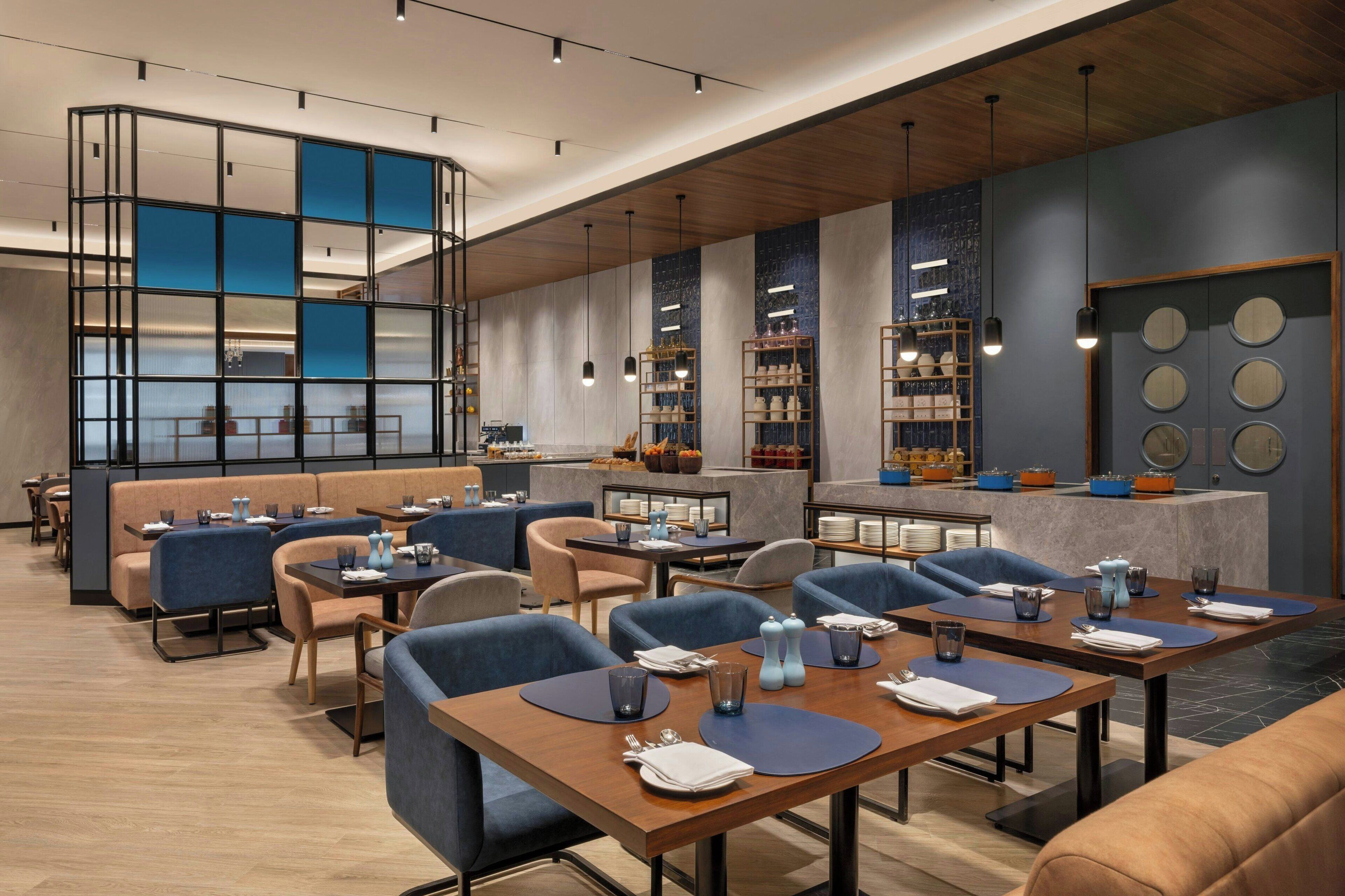 Een modern restaurant met blauwe en beige zitplaatsen, een bar en een decoratieve wand met ronde spiegels.