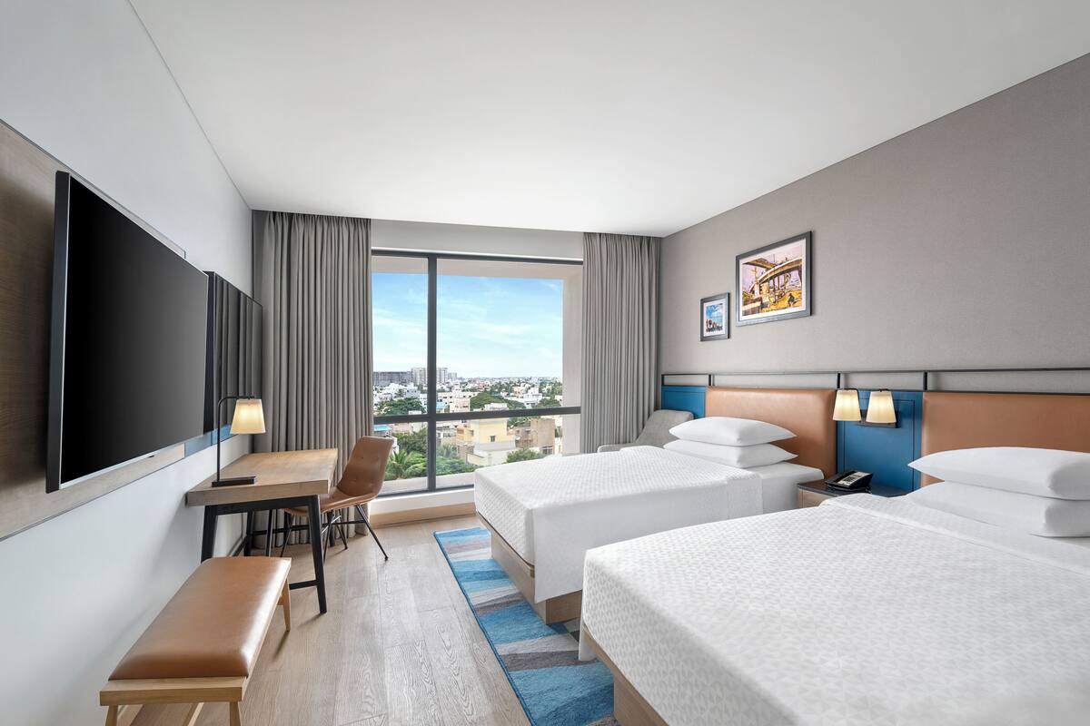Una habitación de hotel con un televisor grande, dos camas, un escritorio y una silla.