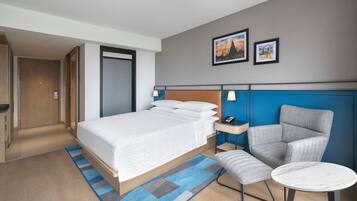A hotel room with a bed, a chair, a small table, a desk, and a door.