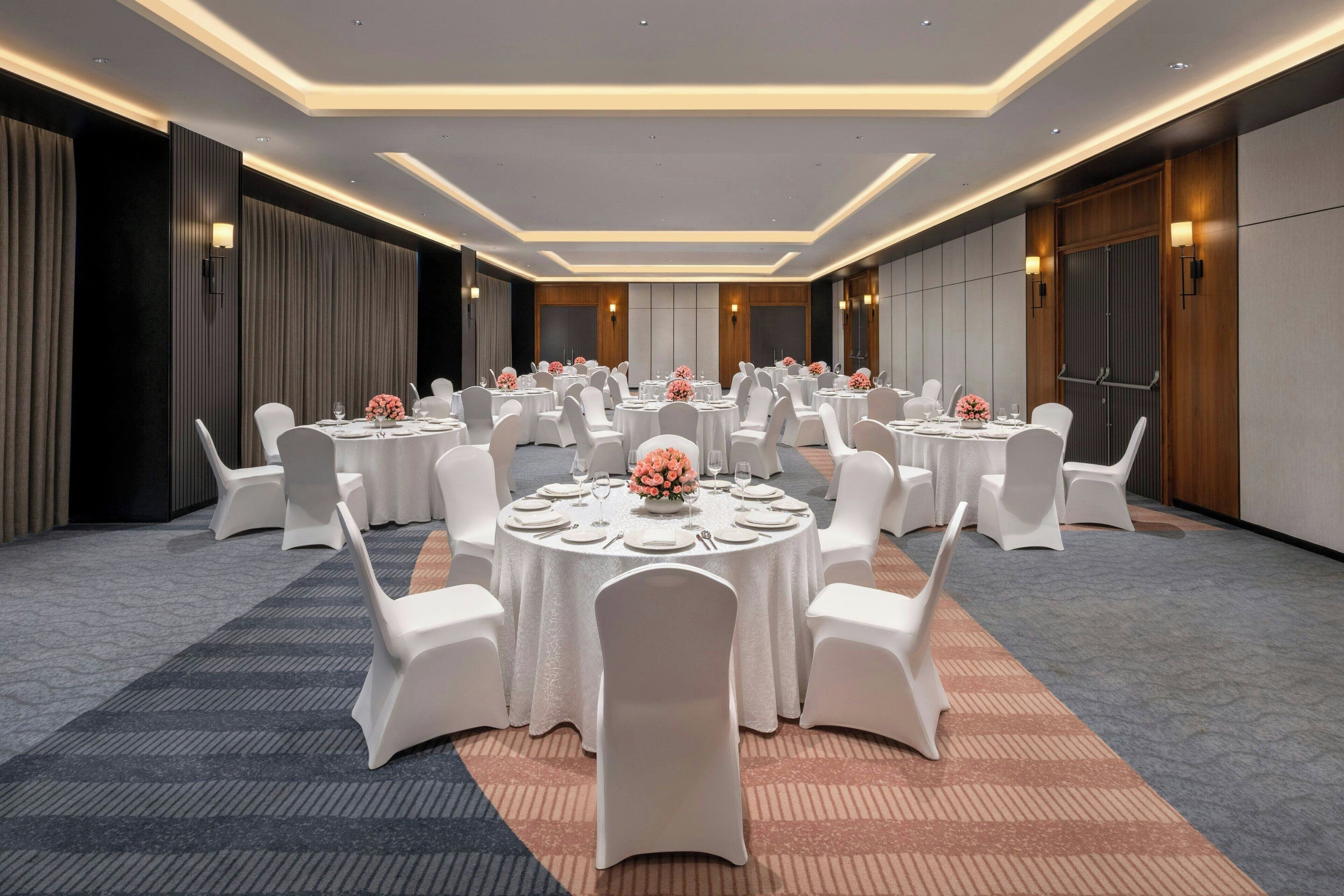 Sala de conferências com mesas redondas, cadeiras brancas e centros de mesa florais.
