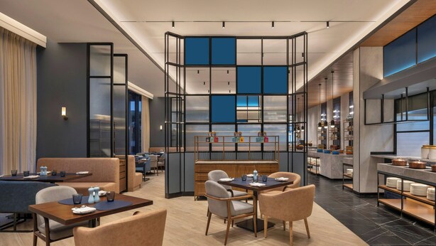 Un moderno vestíbulo de hotel con zonas de estar, un bar central y una cocina a la vista.