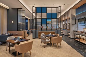 Un moderno vestíbulo de hotel con zonas de estar, un bar central y una cocina a la vista.