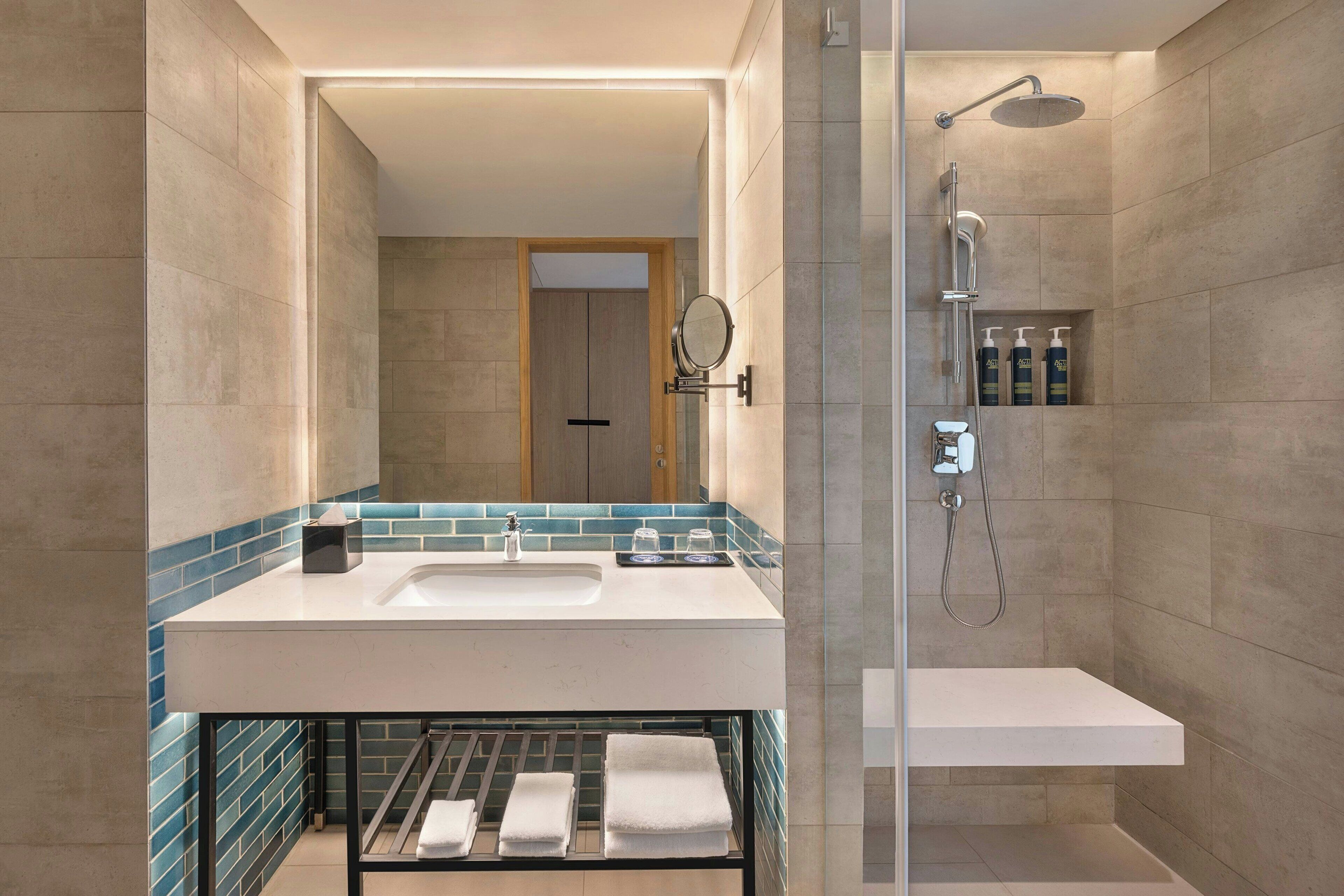 A modern bathroom with a large mirror, a sink, and a shower area.