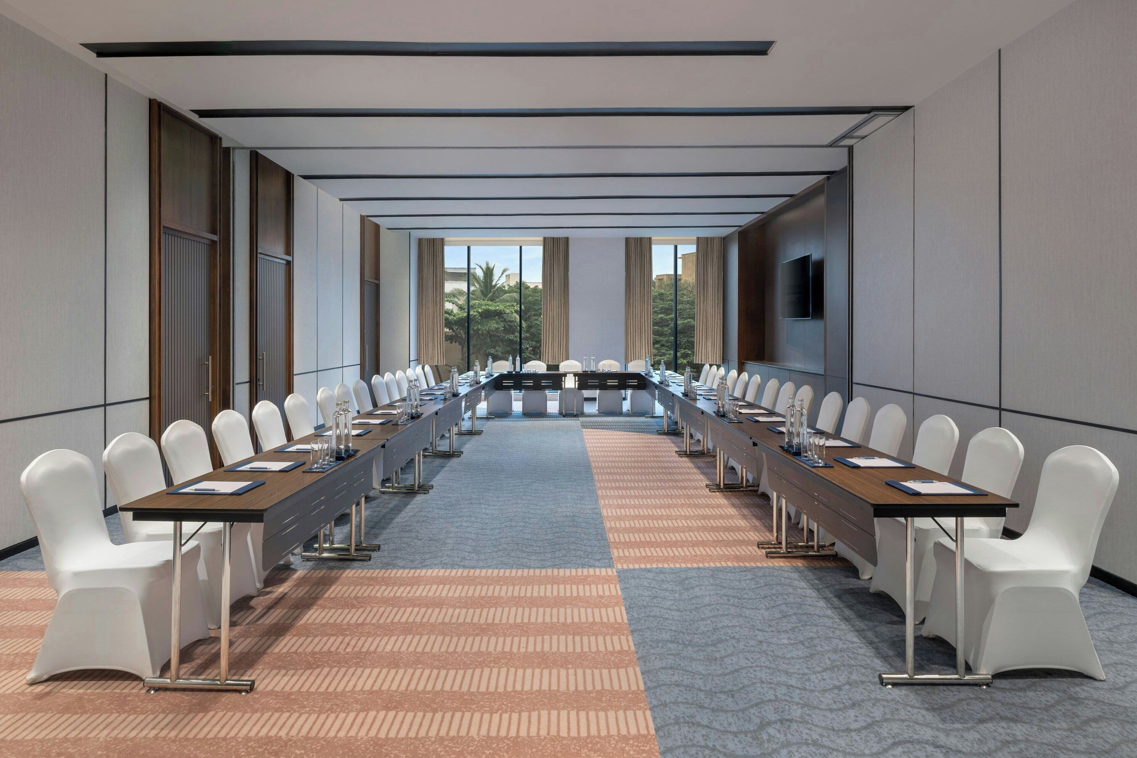 A conference room with a long table, white chairs, and a patterned carpet.