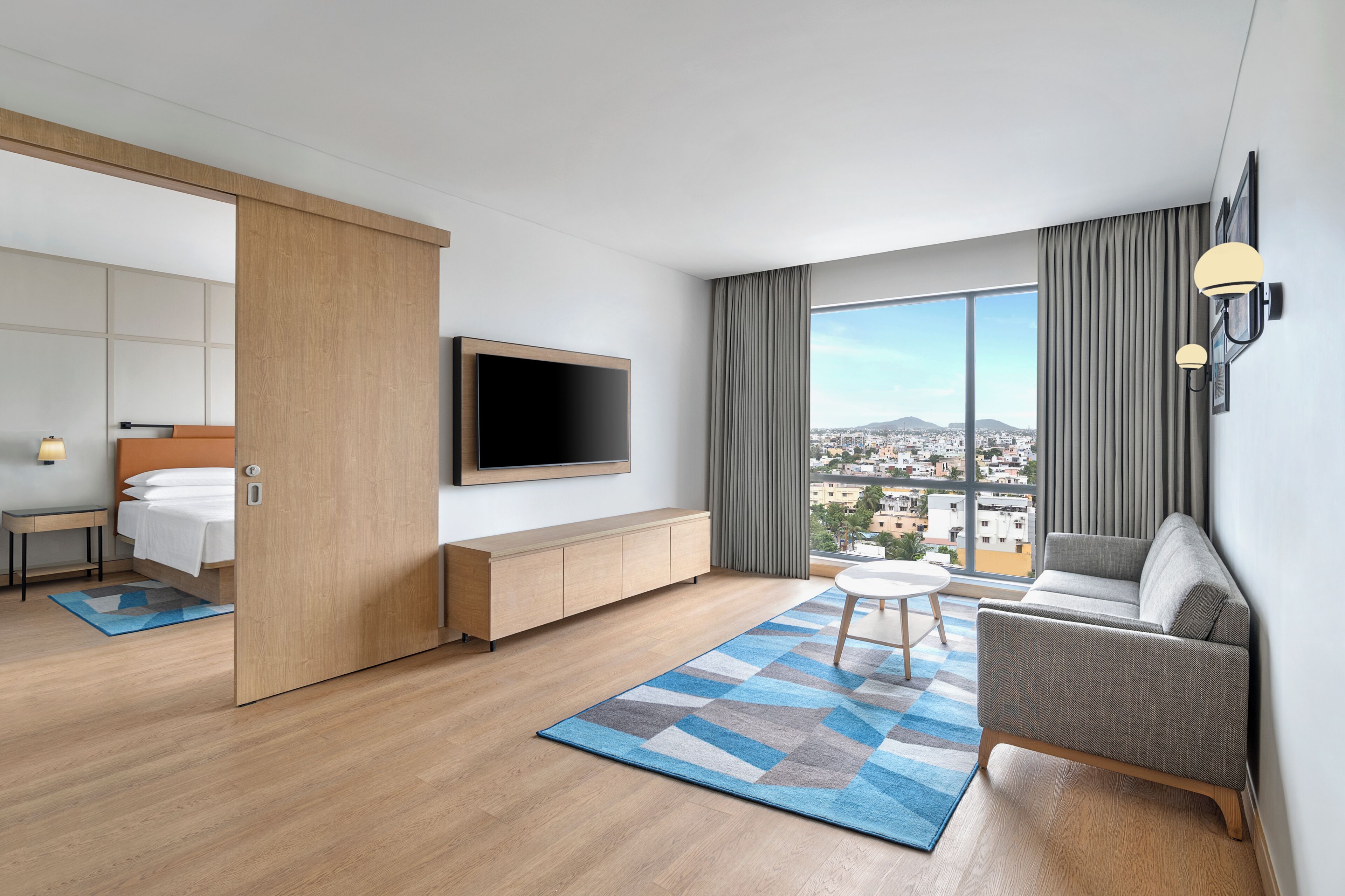Ein modernes Hotelzimmer mit Bett, Fernseher, Sofa und großem Fenster mit Blick auf die Stadt.