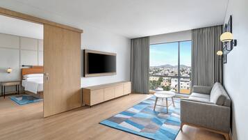 Ein modernes Hotelzimmer mit Bett, Fernseher, Sofa und großem Fenster mit Blick auf die Stadt.
