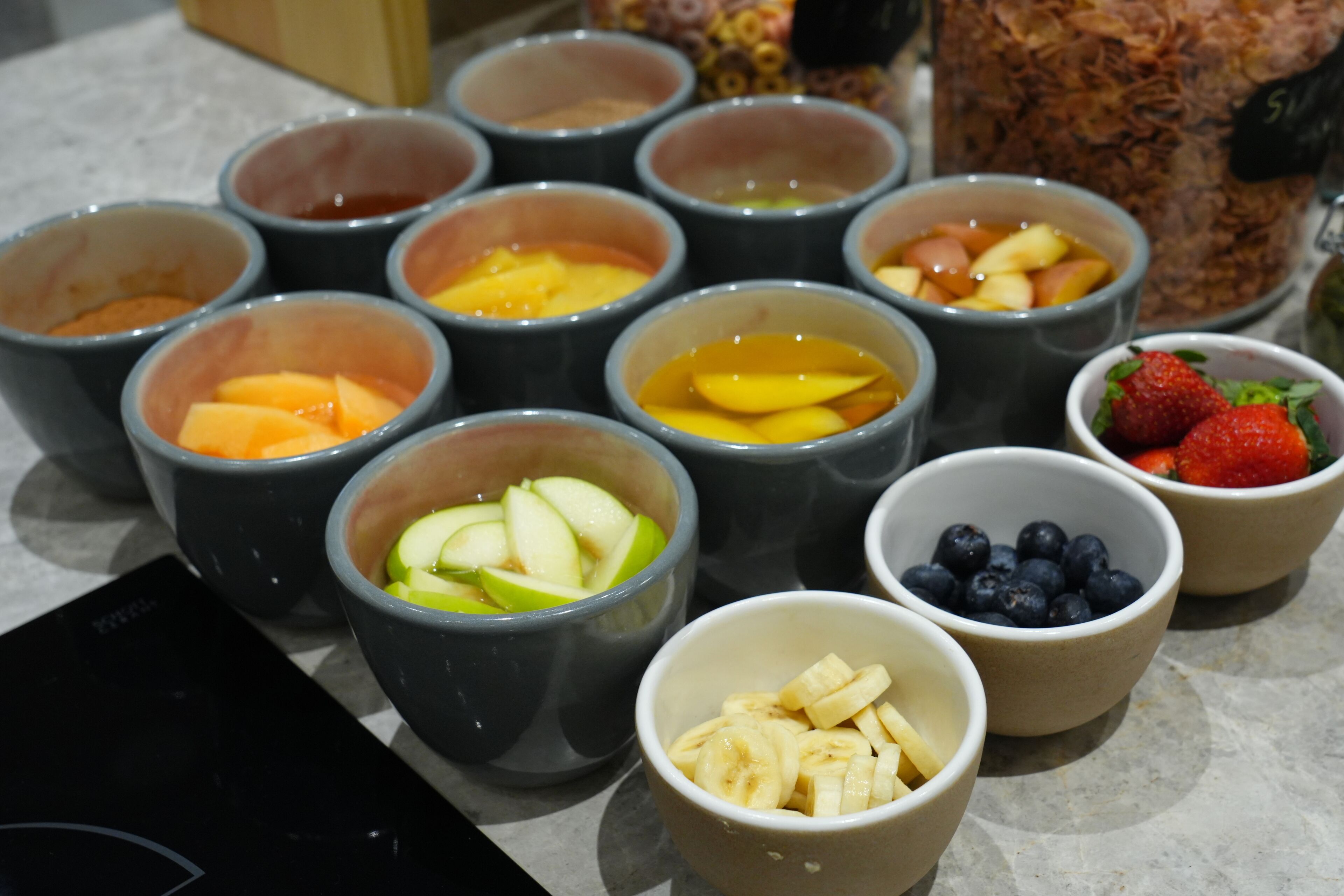 A variety of fruit bowls containing sliced apples, bananas, strawberries, and blueberries.
