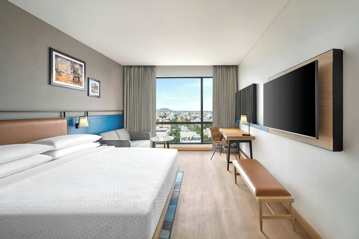 Una habitación de hotel con una cama grande, un escritorio, una silla, un televisor y una ventana con vistas a la ciudad.