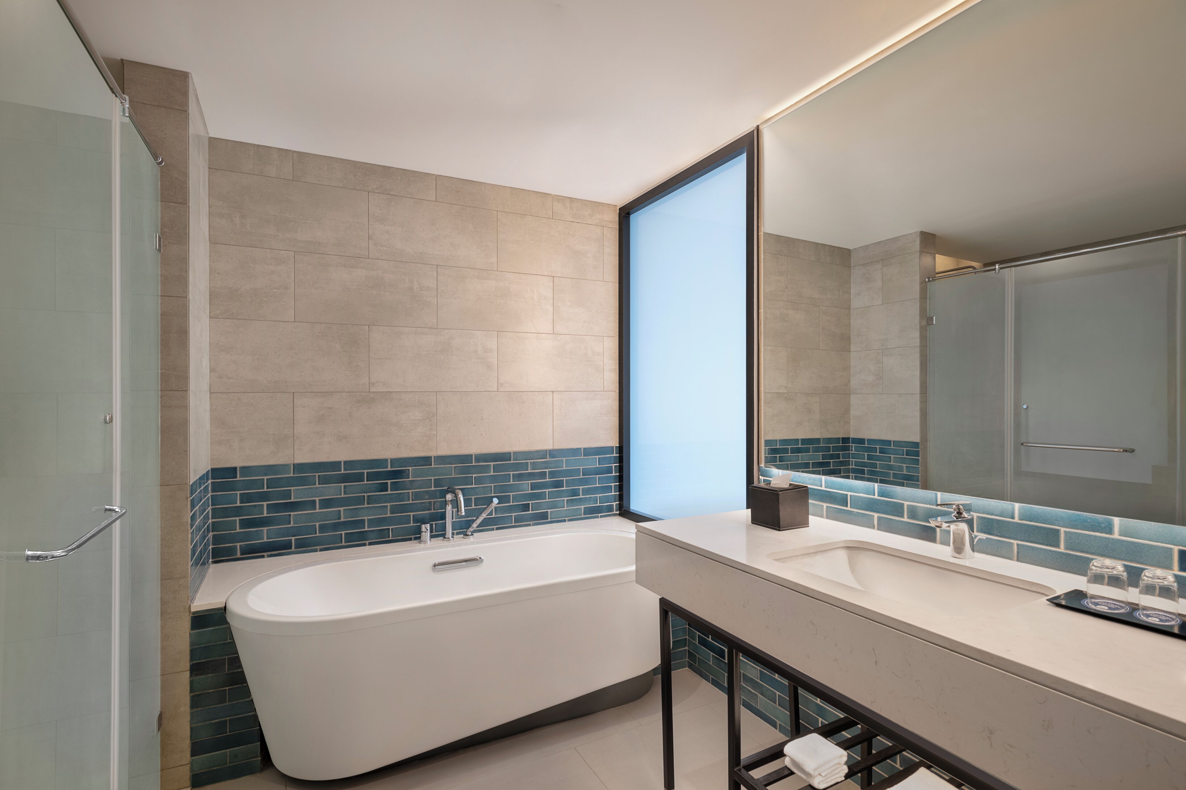 A modern bathroom with a freestanding bathtub, a large mirror, and a tiled backsplash.