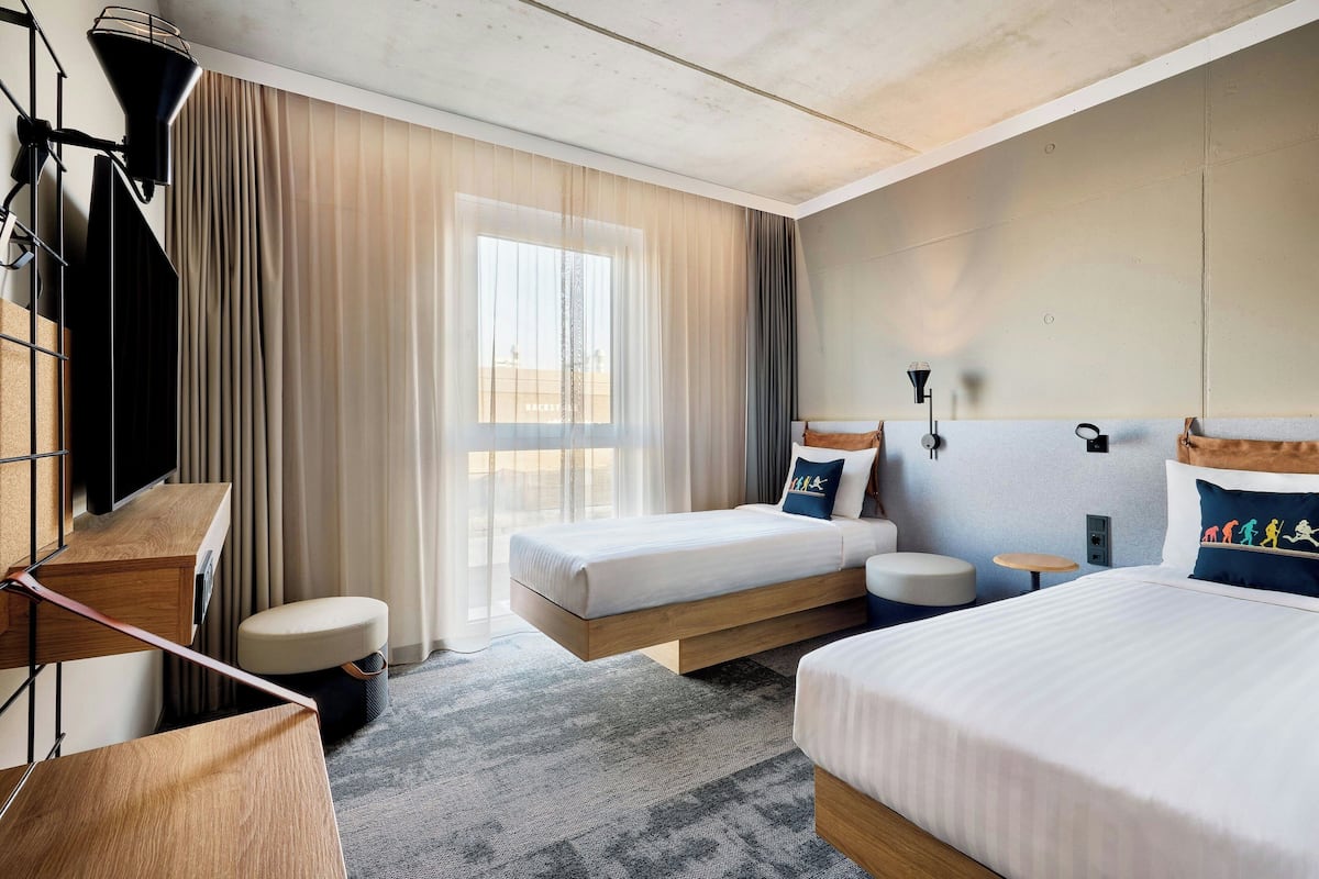 Une chambre d’hôtel avec deux lits, un bureau, une chaise, une télévision et une fenêtre avec des rideaux.