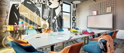 A conference room with a long table, blue and brown chairs, a whiteboard, and a large poster on the wall.
