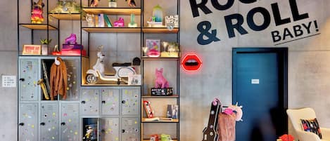 Una habitación con un gran cartel en la pared que dice 'IT'S ONLY ROCK & ROLL BABY!', estantes con varios objetos, una guitarra y una silla blanca.