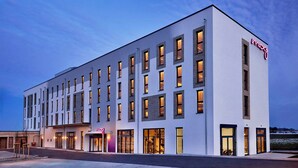 Un hôtel moderne à la façade blanche, doté de nombreuses fenêtres et d’une enseigne lumineuse au néon.