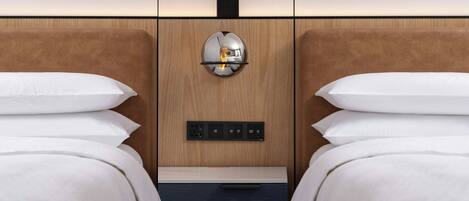 A hotel room with two beds, a wooden headboard, a wall-mounted light fixture, and a control panel.
