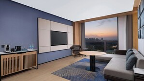 Una habitación de hotel moderna con un ventanal grande, un televisor de pantalla plana, un sofá, una mesa redonda y una consola de madera.