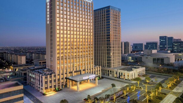 Un hotel de gran altura con un llamativo letrero de 'Four Points by Sheraton', que presenta un diseño arquitectónico moderno con un amplio frente de vidrio.