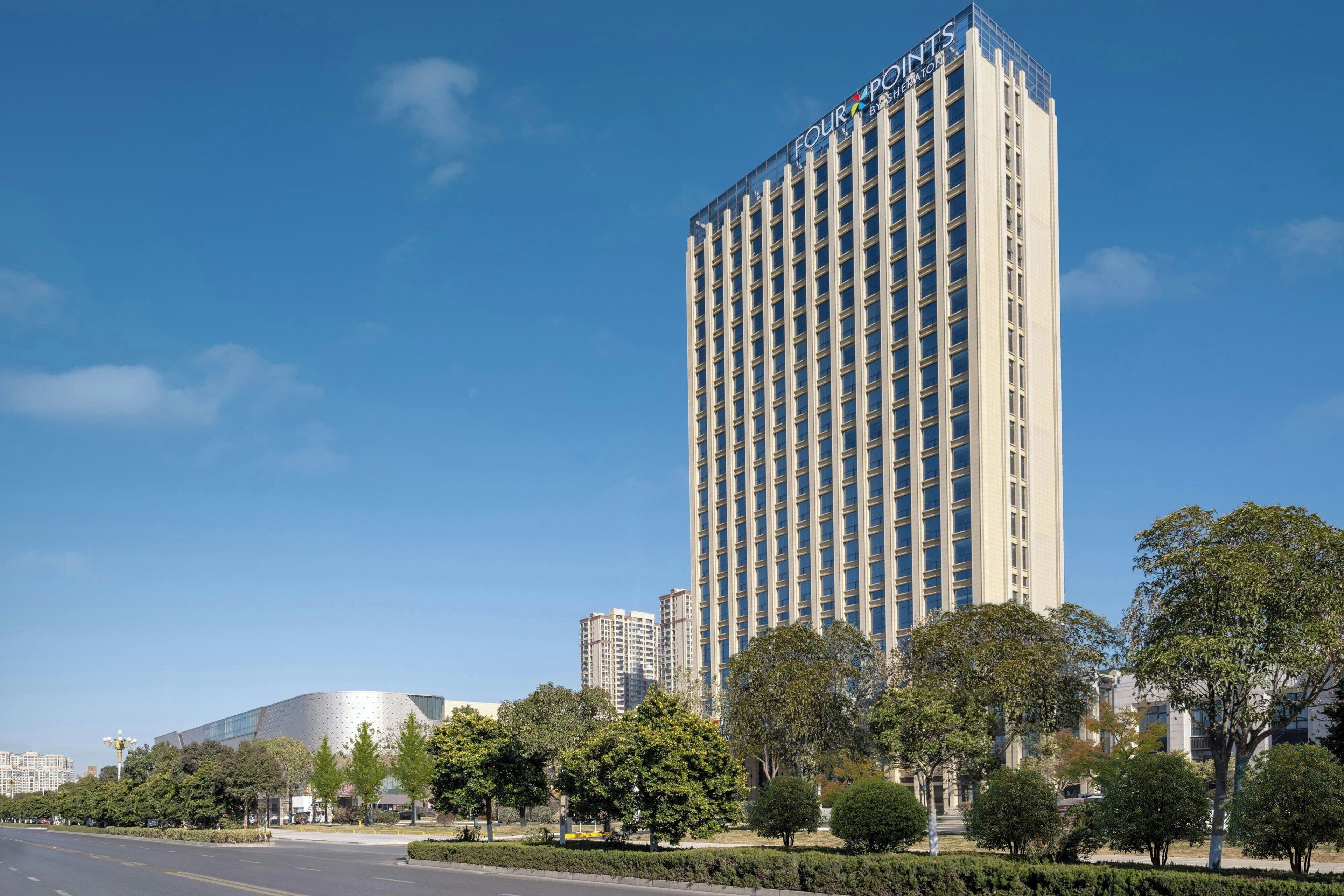 Un edificio de hotel alto de diseño moderno, rodeado de árboles y un cielo azul despejado.