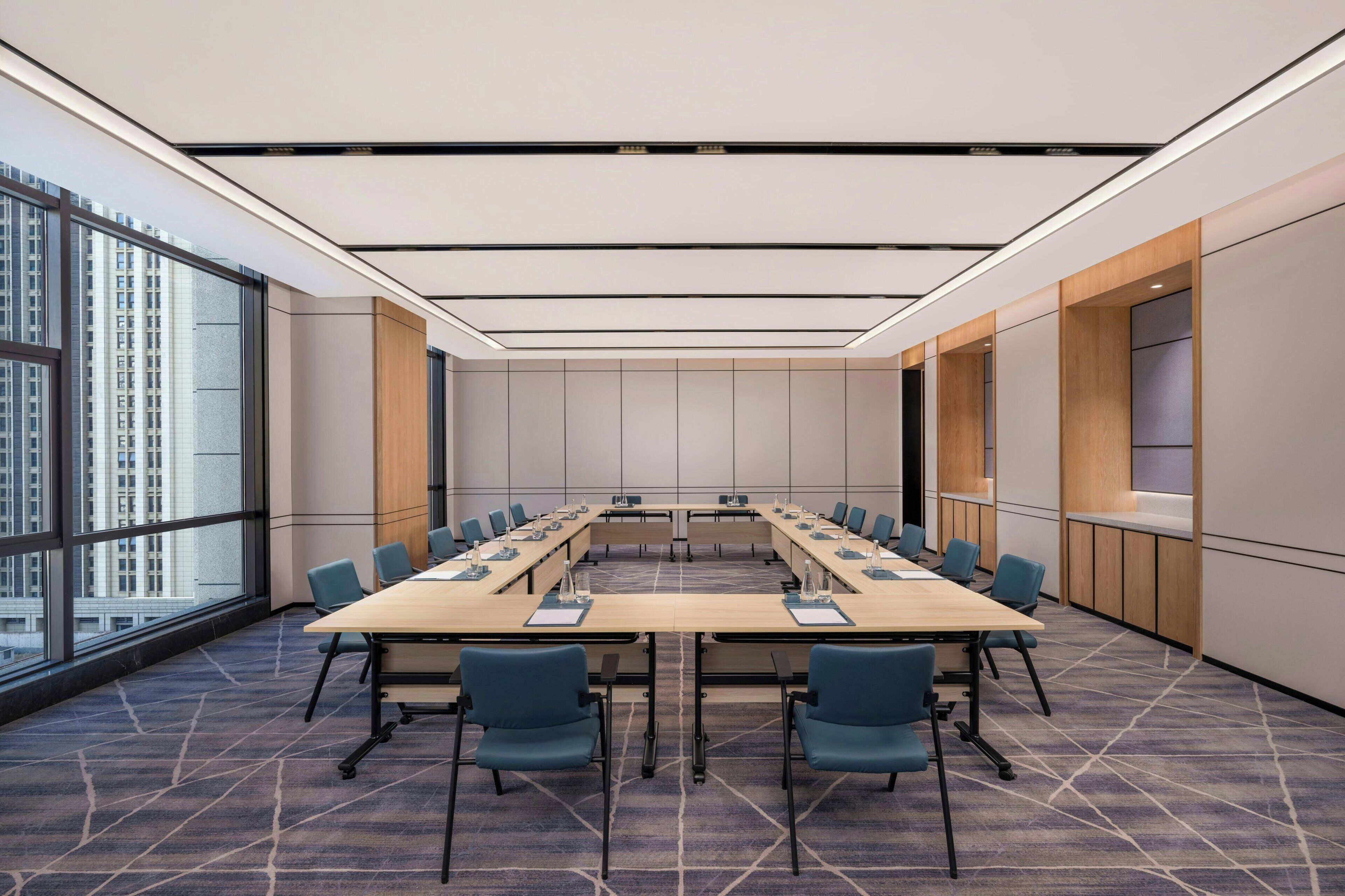 Une salle de conférence avec une longue table, des chaises bleues et un sol recouvert de moquette.