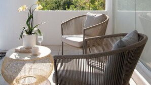 A balcony with wicker furniture, a potted plant, and a view of a green landscape.