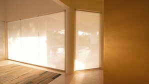 A room with a sliding glass door leading to a balcony, a wooden floor mat, and a plain wall.