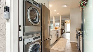 Een moderne keuken met een ingebouwde wasmachine en droger, een eethoek en uitzicht op de woonkamer.