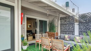 Een terras buiten met een houten tafel en stoelen, een bank en een decoratief scherm.