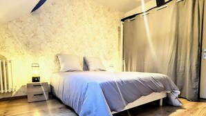 A bedroom with a bed, a nightstand, a lamp, and a window with curtains. - "La Citadelle - Duplex with view of Château-fort (Sedan)