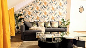 A modern living room with a sofa, a glass coffee table, and a patterned wallpaper. - "La Citadelle - Duplex with view of Château-fort (Sedan)