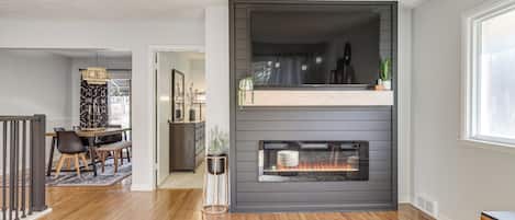 A modern living room with a fireplace, wooden flooring, and a dining area with a table and chairs.
