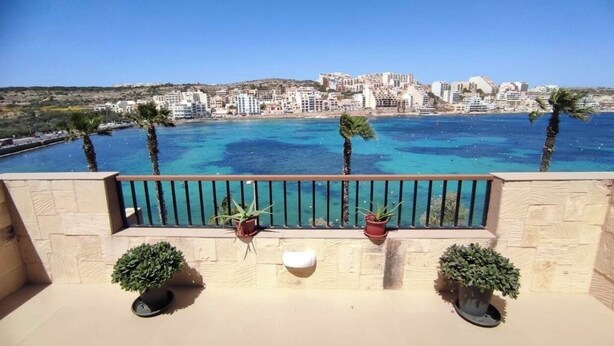 Un balcon offrant une vue sur un paysage urbain côtier, avec une mer bleue et des palmiers.