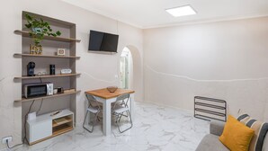 A compact living space with a kitchenette, a dining area, a TV mounted on the wall, and a small seating area with cushions. - Elegant tourist accommodation facing metro C (Roma)