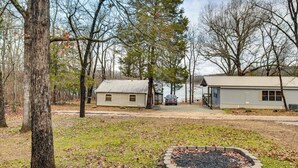 A cabin with a stone fire pit, surrounded by trees and a lake. - Norfork Lake Access: Cabin w/ Deck & Water View! (Elizabeth)