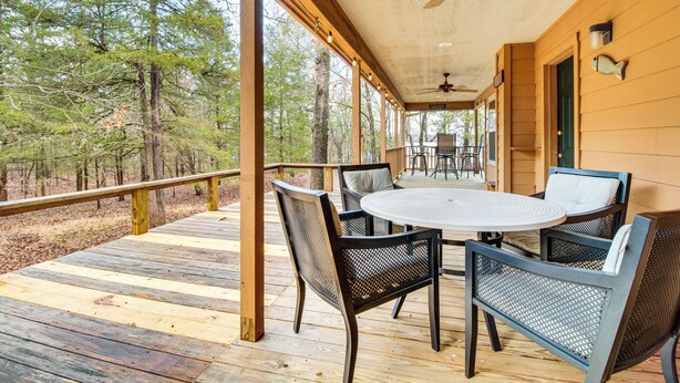 A covered wooden deck with a round table and chairs, surrounded by trees. - Norfork Lake Access: Cabin w/ Deck & Water View! (Elizabeth)