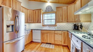 A kitchen with wooden cabinets, stainless steel appliances, a clock, and a window. - Norfork Lake Access: Cabin w/ Deck & Water View! (Elizabeth)