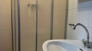 A bathroom with a glass shower enclosure, a white sink with a chrome faucet, and a tiled floor. - HS Hotel (Hamburg)