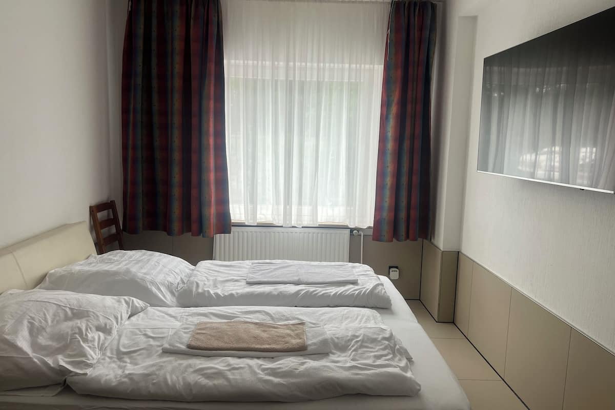 A hotel room with two beds, a radiator, and a window with curtains.