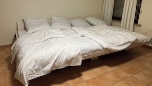 A bed with white bedding in a room with tiled flooring and a window with curtains. - HS Hotel (Hamburg)
