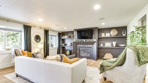 Un salon comprenant un canapé, un fauteuil, une cheminée, un téléviseur et des objets de décoration.